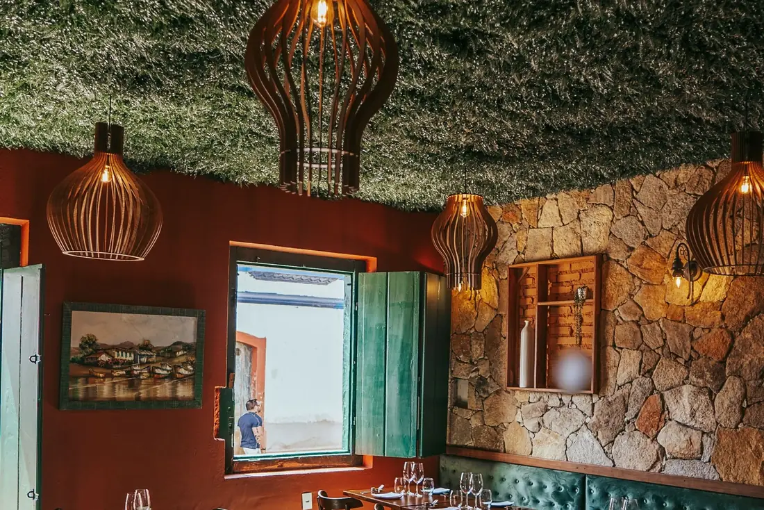 Salle de restaurant dressée, suspensions en bois et mur de pierre.